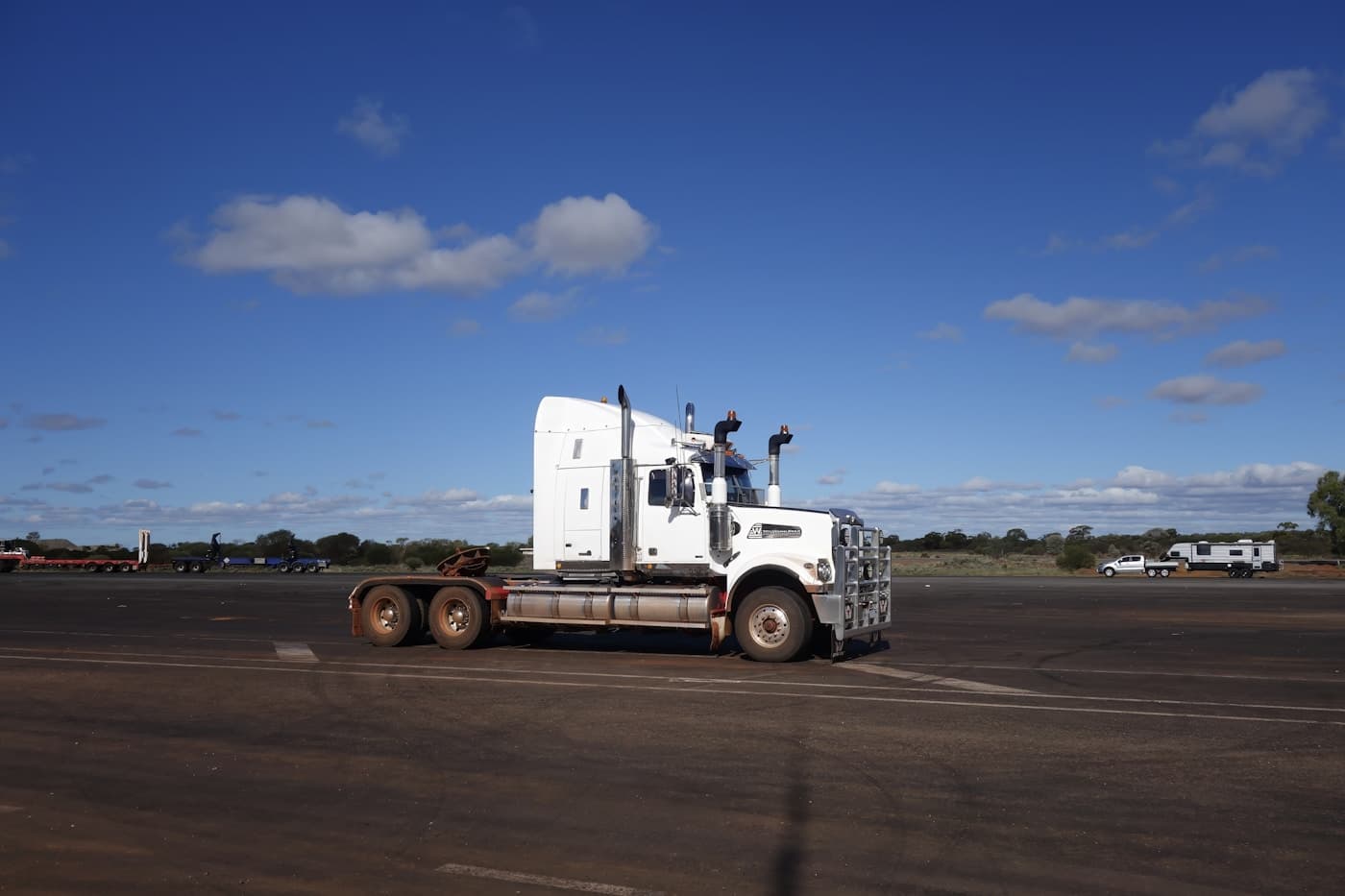 A white tractor unit parked on open tarmac under a clear sky.